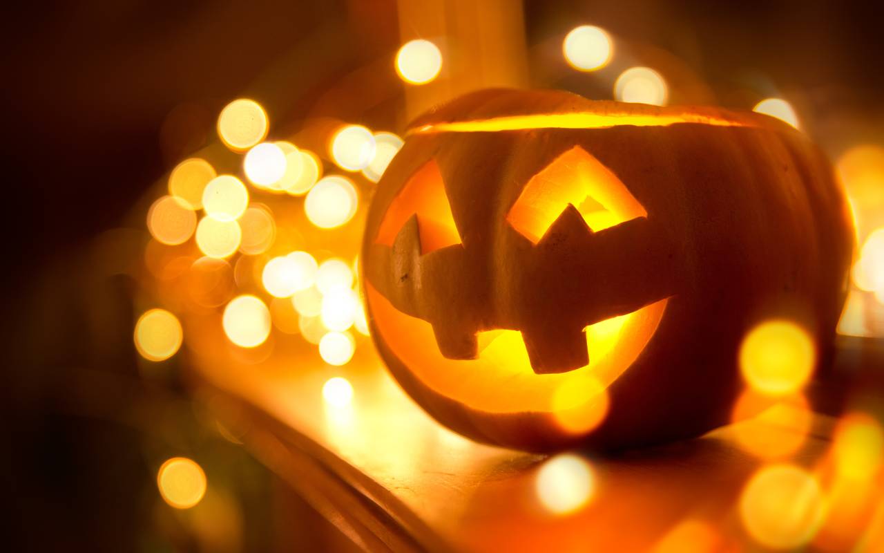 Ein fröhlich lächelnder Jack O’Lantern steht zu Halloween auf einem Kamin, umgeben von Lichterketten.