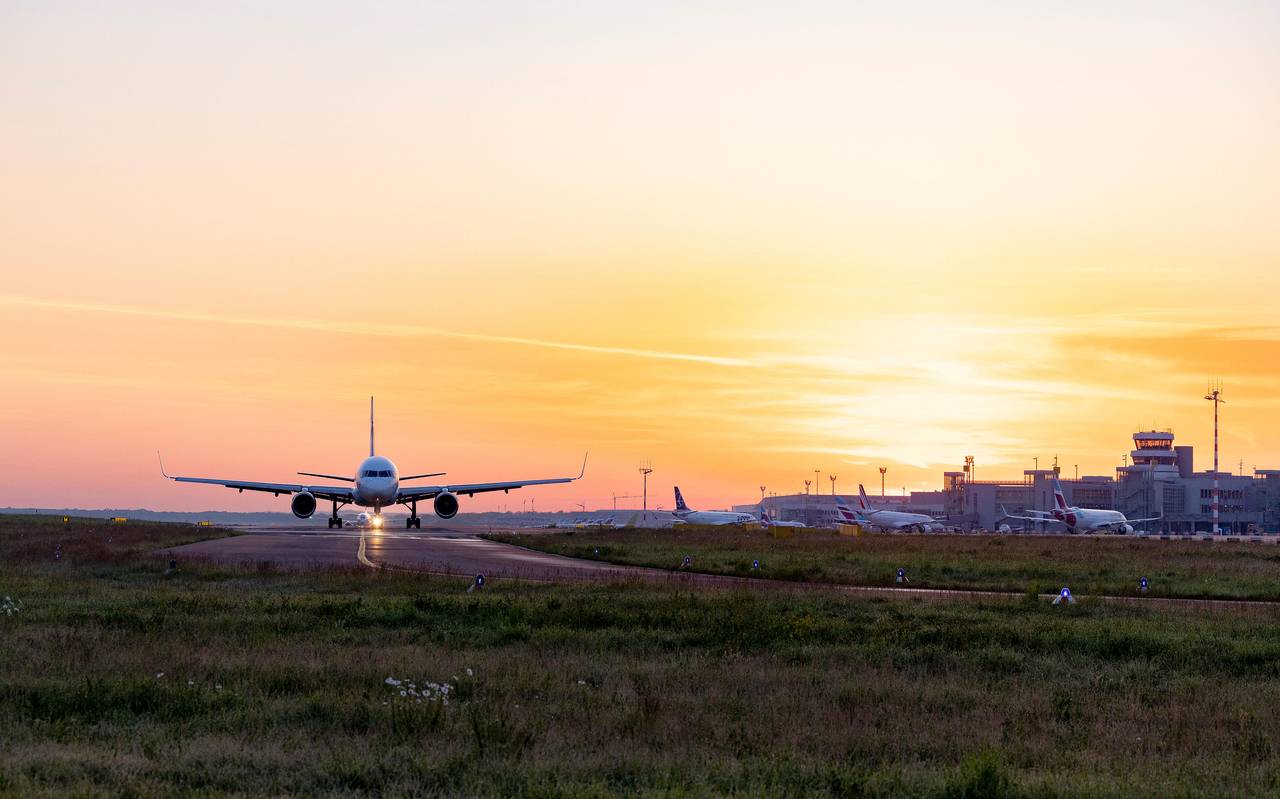 Ein Flugzeug steht auf dem Rollfeld des Düsseldorfer Flughafens vor einem Sonnenuntergang oder -aufgang.