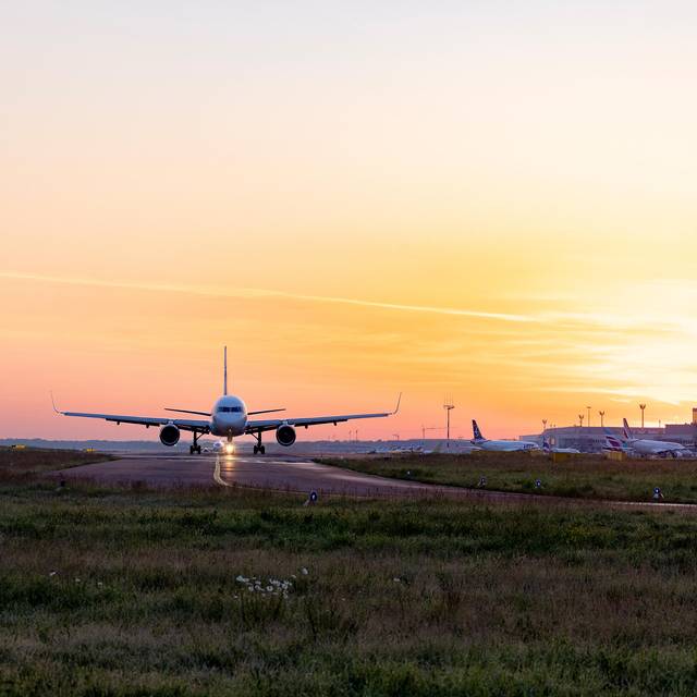 Ein Flugzeug steht auf dem Rollfeld des Düsseldorfer Flughafens vor einem Sonnenuntergang oder -aufgang.