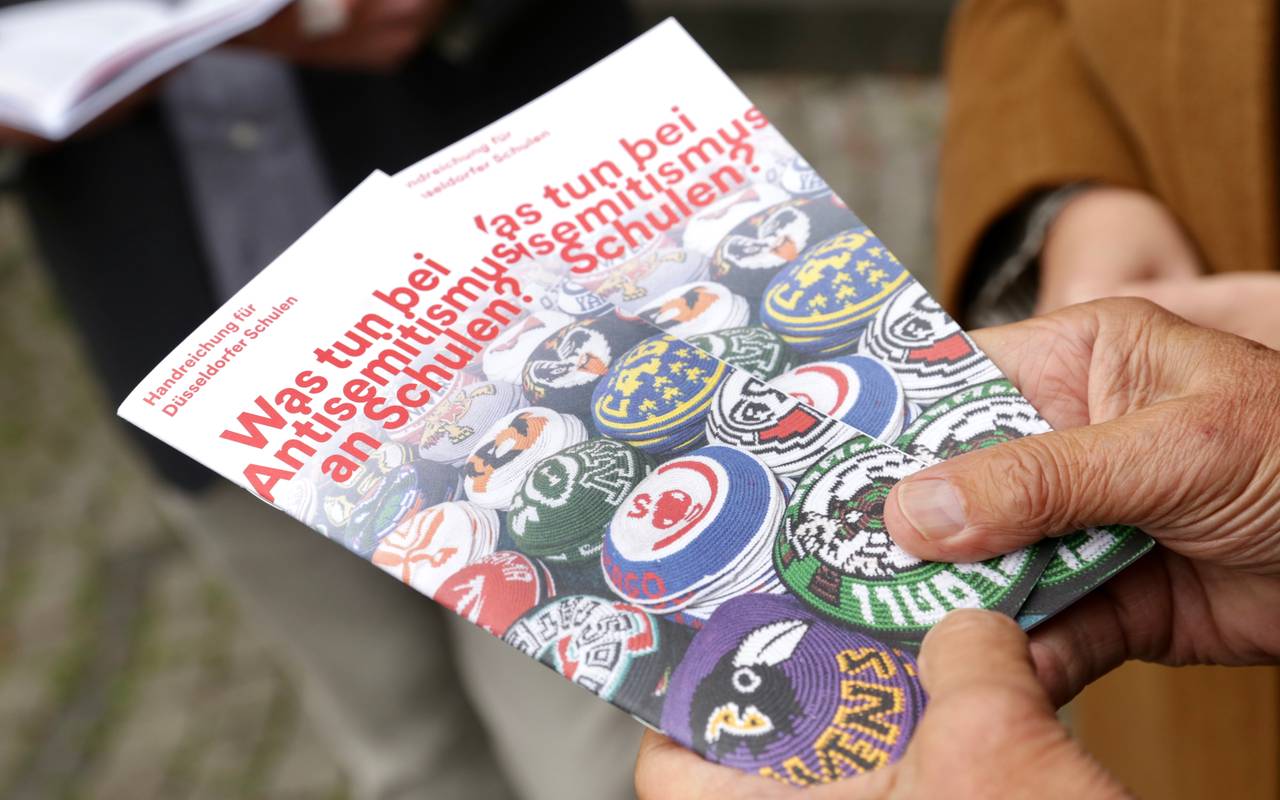 Zwei Hände halten zwei Exemplare der Broschüre "Was tun bei Antisemitismus?" in die Kamera