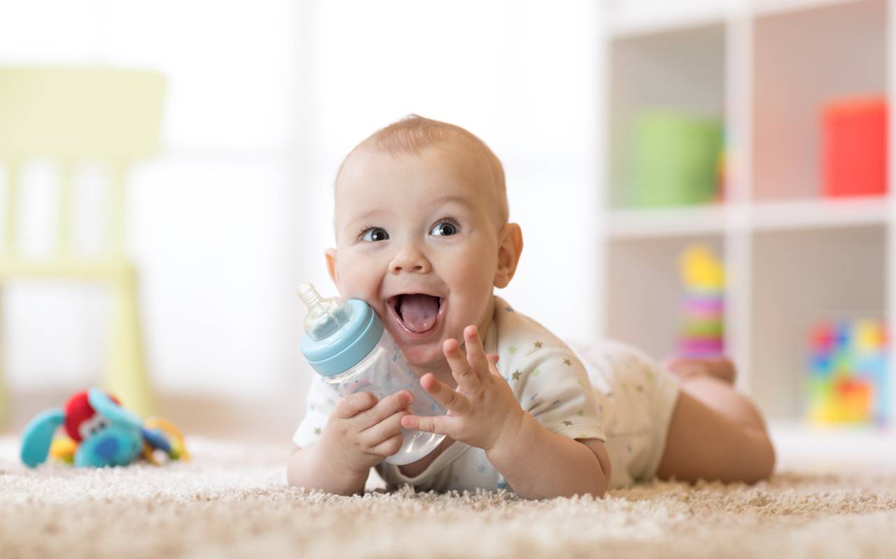 Lächelnder Säugling (7 Monate alt) trinkt aus einer Babyflasche.