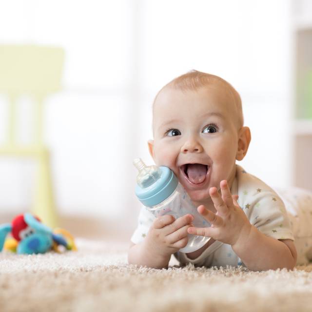 Lächelnder Säugling (7 Monate alt) trinkt aus einer Babyflasche.