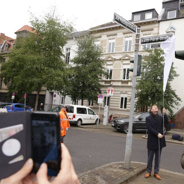 OB Keller enthüllt die neuen Straßenschilder "Am Polizeipräsidium" und "Edith-Fürst-Straße". Viele Nachbarn und Fotografen beobachten die Aktion auf dem ehemaligen Jürgensplatz.