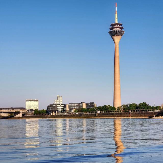 Der Rheinturm bei bestem Wetter. Er spiegelt sich sogar im Rhein.
