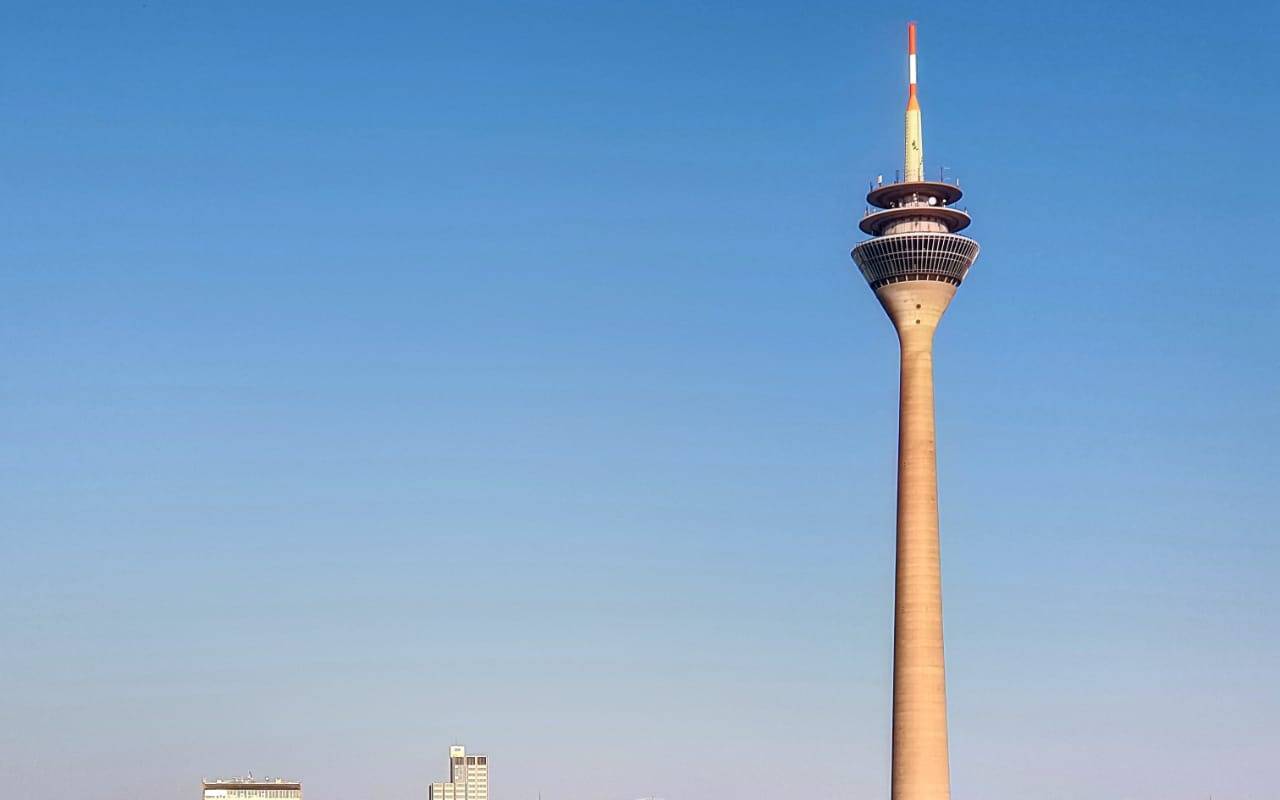 Der Rheinturm bei bestem Wetter. Er spiegelt sich sogar im Rhein.