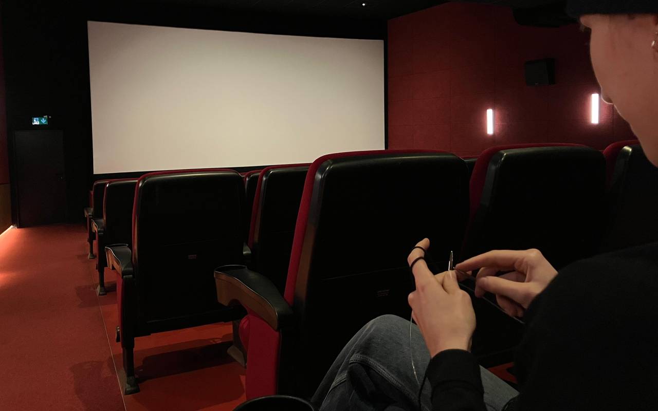 In einem leeren Kinosaal sitzt im Vordergrund eine junge Frau und strickt.