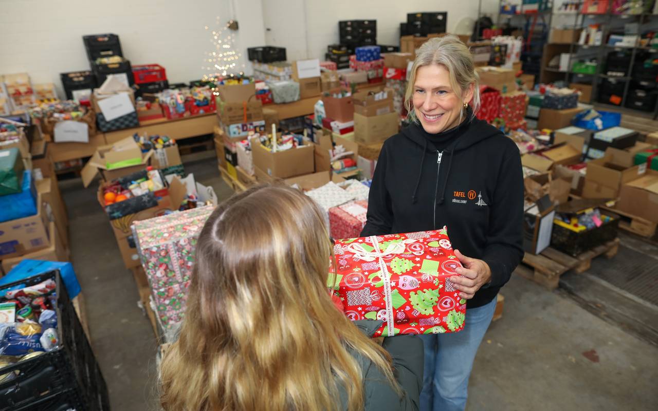 Tafel-Vorständin Eva Fischer übergibt ein Weihnachtspäckchen. In der Halle liegen viele weitere gespendete Päckchen.