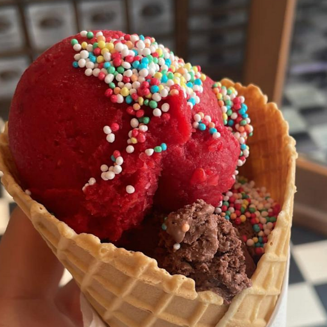 Eine rote Eiskugel mit Streuseln in einem Hörnchen.