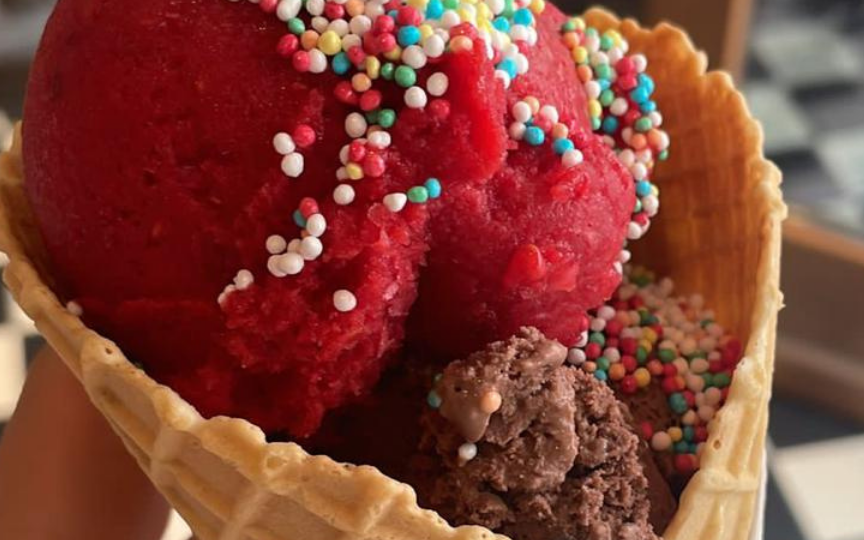 Eine rote Eiskugel mit Streuseln in einem Hörnchen.