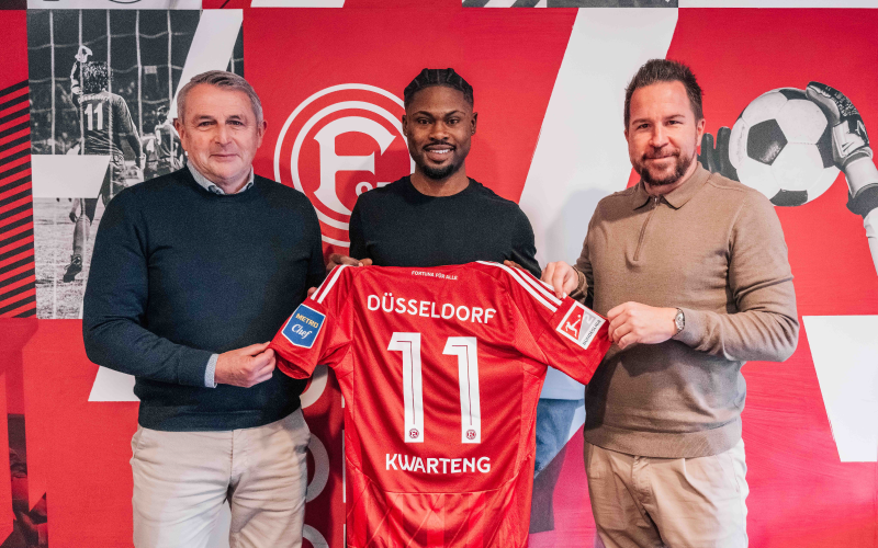 Bei der Vorstellung von Fortuna-Neuzugang Kwarteng stehen Moritz Kwarteng (mitte), Klaus Allofs (links) und Christian Weber (rechts) vor einer Wand und halten ein rotes Fortuna Trikot mit der Nummer 11 hoch.