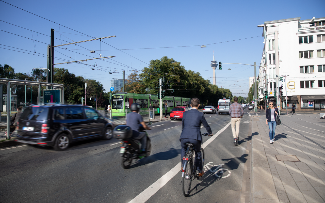 Das Foto zeigt verschiedene Formen der Mobilität am Graf-Adolf-Platz. Neben der Bahn fahren Autos. Außerdem sind Radfahrer auf einem Fahrradstreifen unterwegs und Fußgänger laufen über den Bürgersteig.