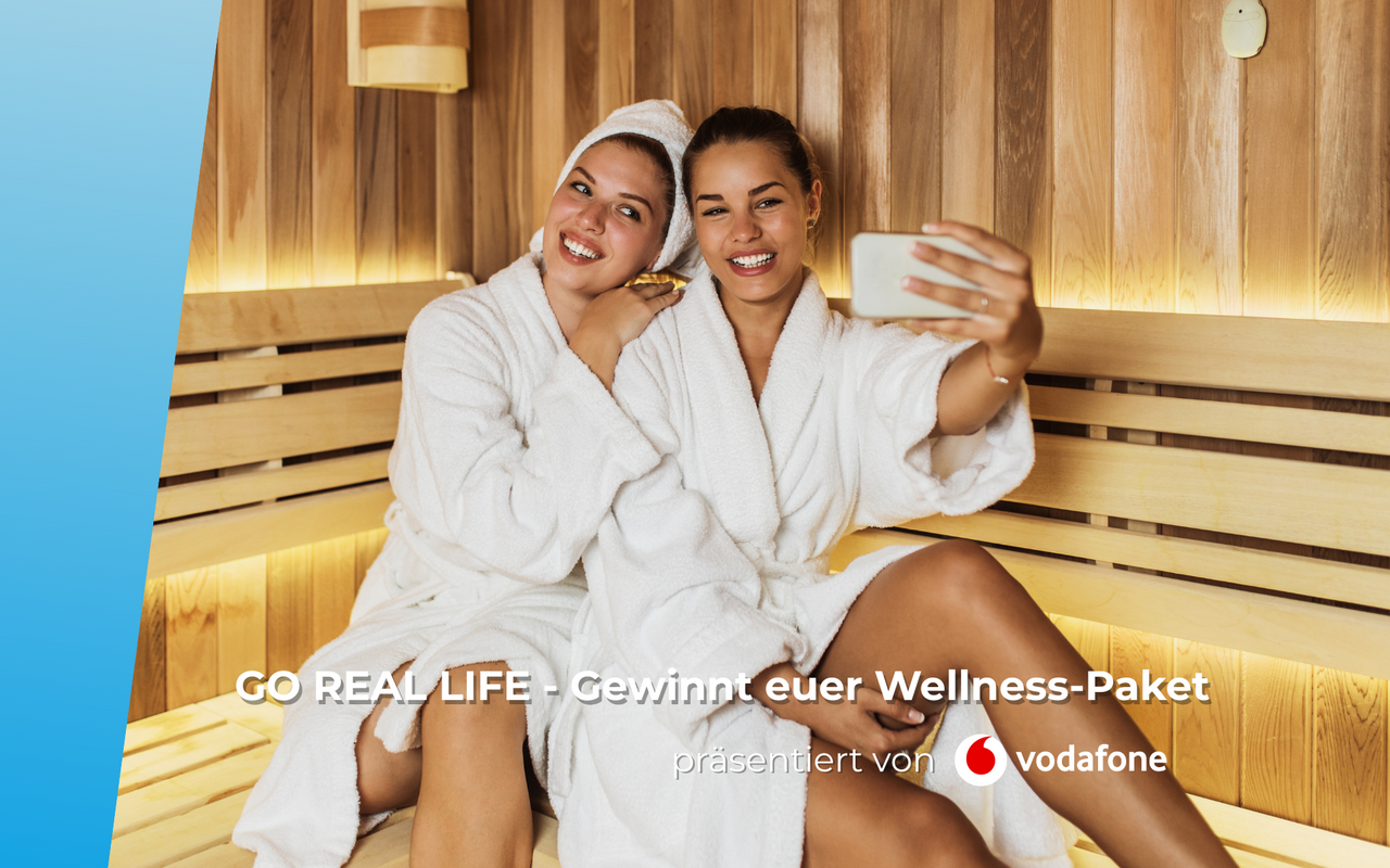 Zwei Damen im Bademantel sitzen gemeinsam in der Sauna und machen ein Selfie von sich.