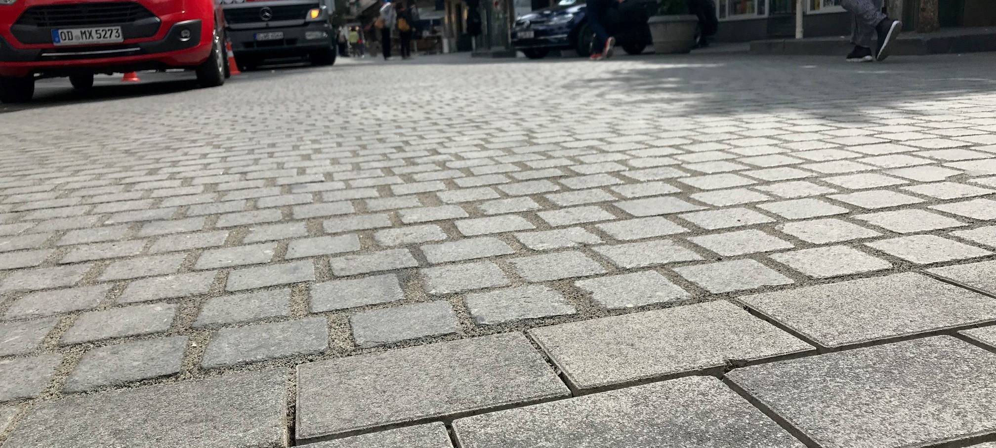 Das Bodenpflaster der Bolkerstraße. Im Hintergrund stehen LKW.