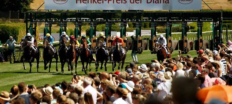 Mehrere Jockeys und Zuschauer beim Henkel-Renntag auf der Galopprennbahn.