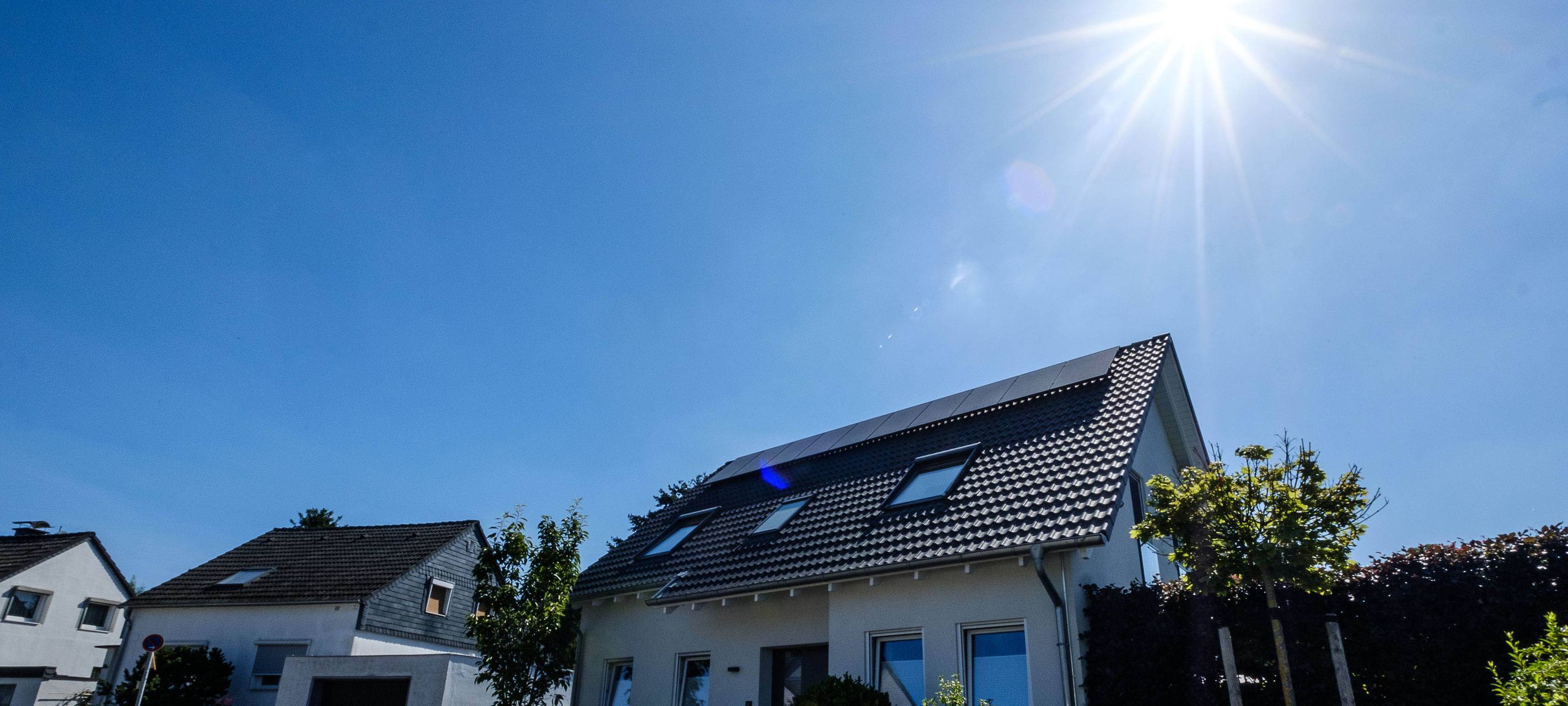 Wohnhaus mit Solaranlage auf dem Dach. Im Hintergrund sind zwei weitere Häuser zu sehen.