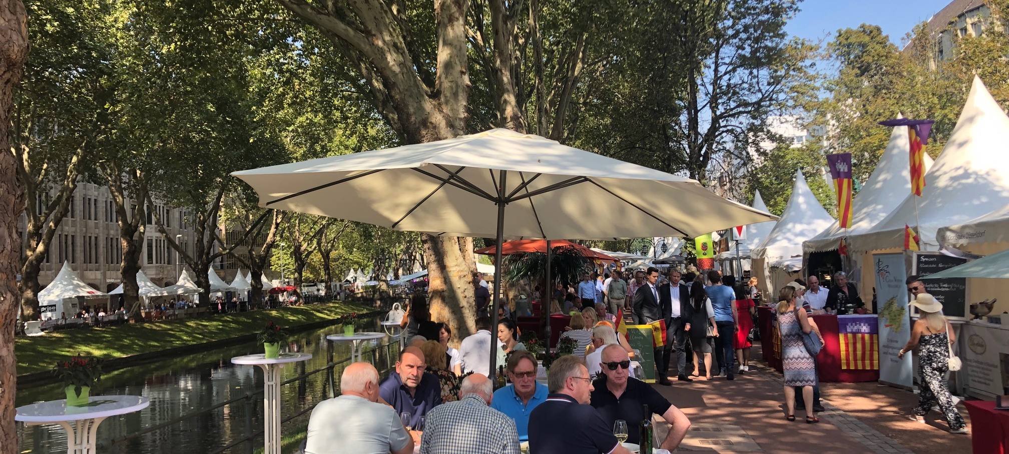 Mehrere Menschen sitzen auf Bierbänken, im Hintergrund ist der Kögraben zu sehen. Es ist das Gourmet Festival.