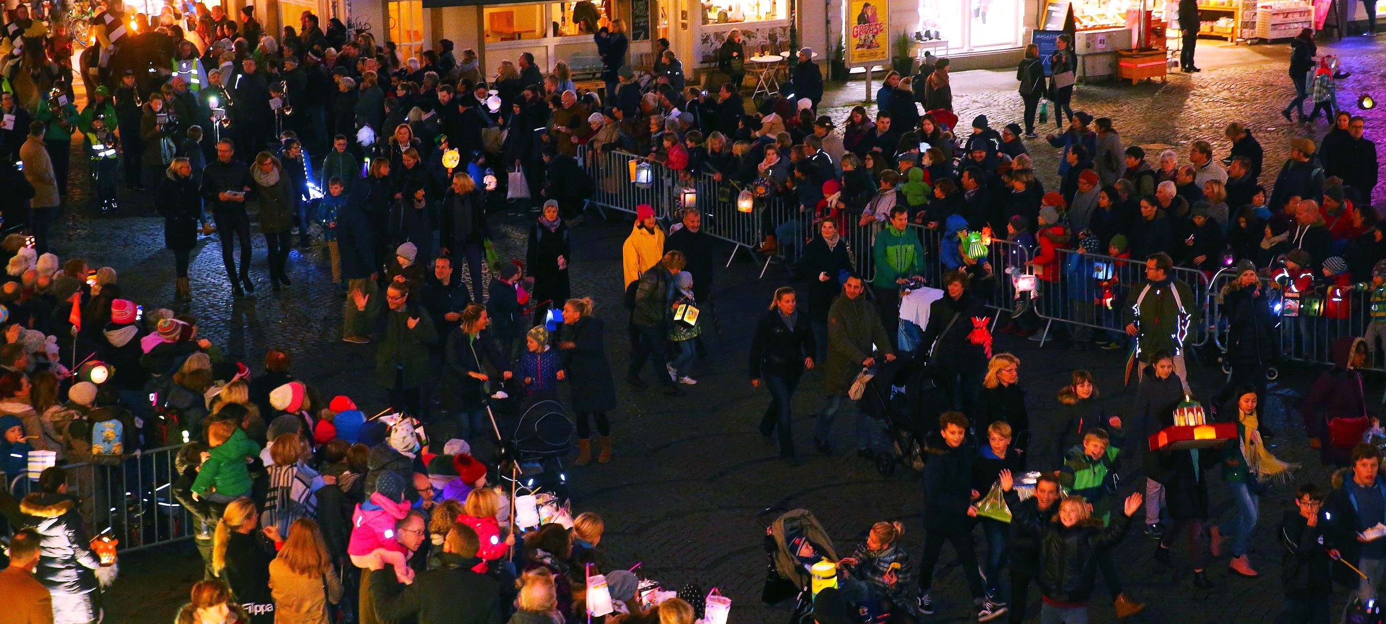 Auf dem Marktplatz warten Kinder mit leuchtenden Laternen auf St. Martin und die Mantelteilung.