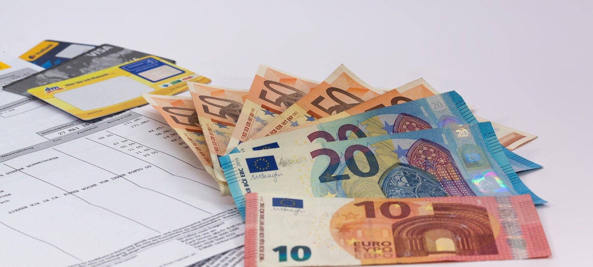 Geldscheine liegen auf einer weißen Fläche. Zu sehen sind auch Rechnungen und EC- und Kreditkarten.