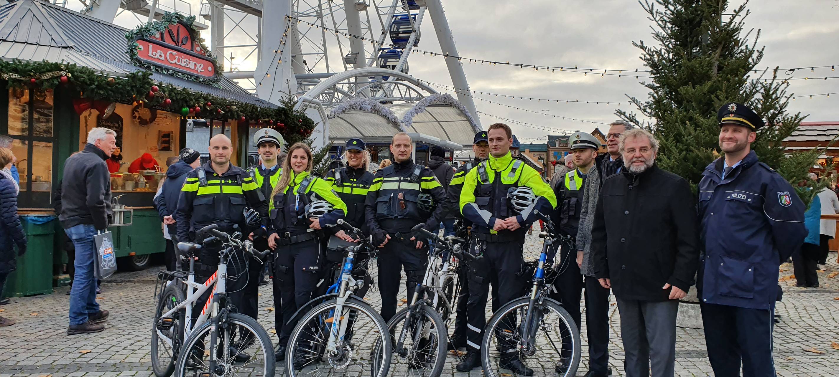 Deutsche und niederländische Polizeibeamte stehen mit Fahrrädern vor dem Riesenrad am Burgplatz.