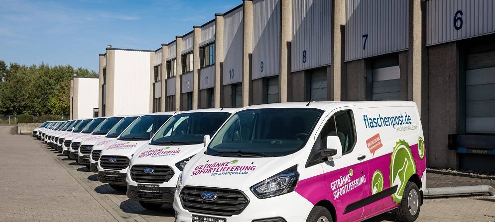 Mehrere Flaschenpost-Transporter stehen vor einer Halle.