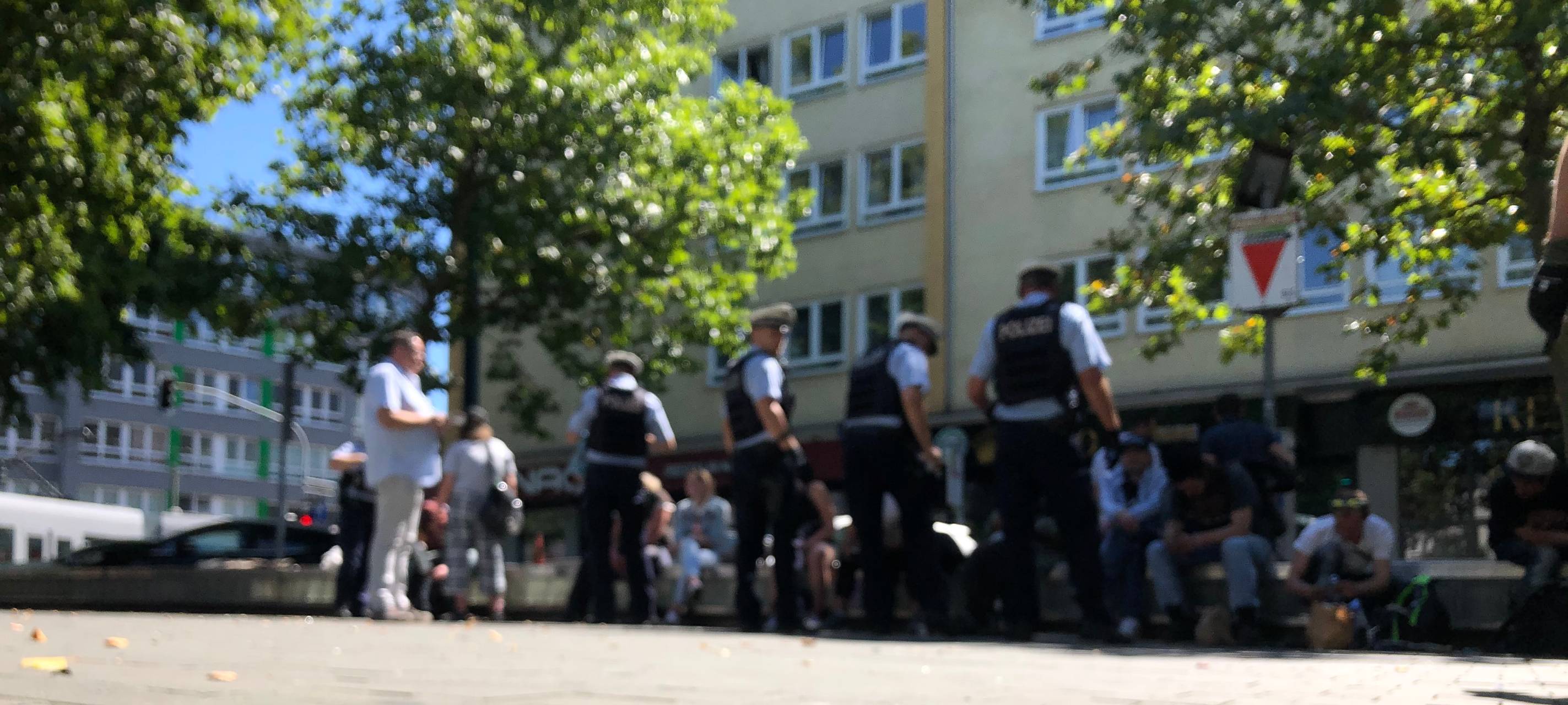 Polizisten im Einsatz auf dem Worringer Platz. Sie kontrollieren Personen, die auf Bänken sitzen.