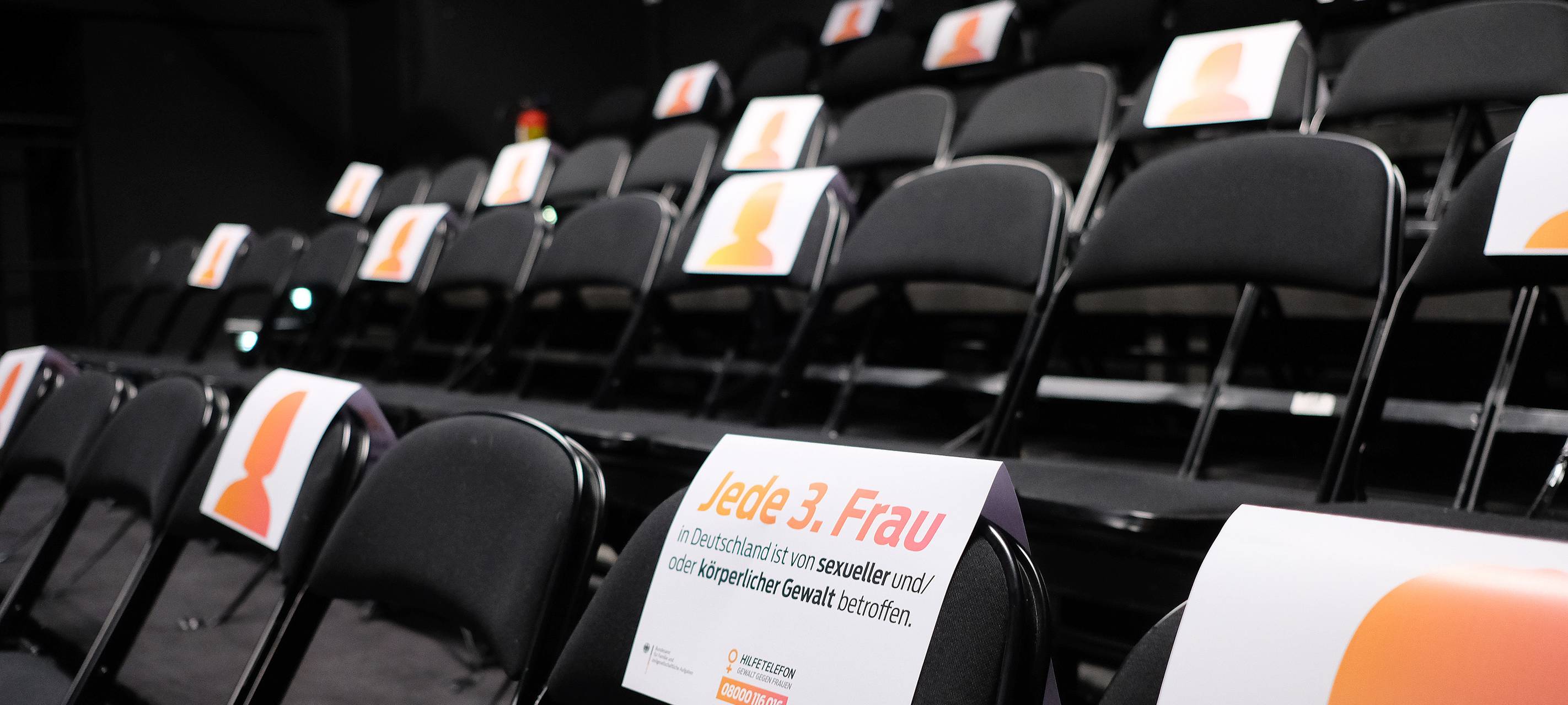 Leere Stühle in in einem Auditorium. Jeder dritte Sitz ist mit einem Schild markiert. Das soll auf Gewalt gegen Frauen aufmerksam machen.