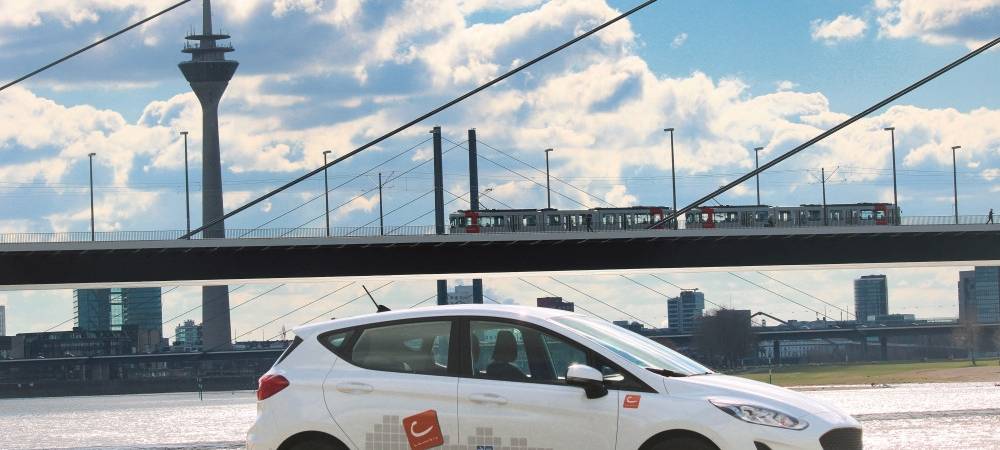 Weißes Car-Sharing-Auto steht vor der Oberkasseler Brücke