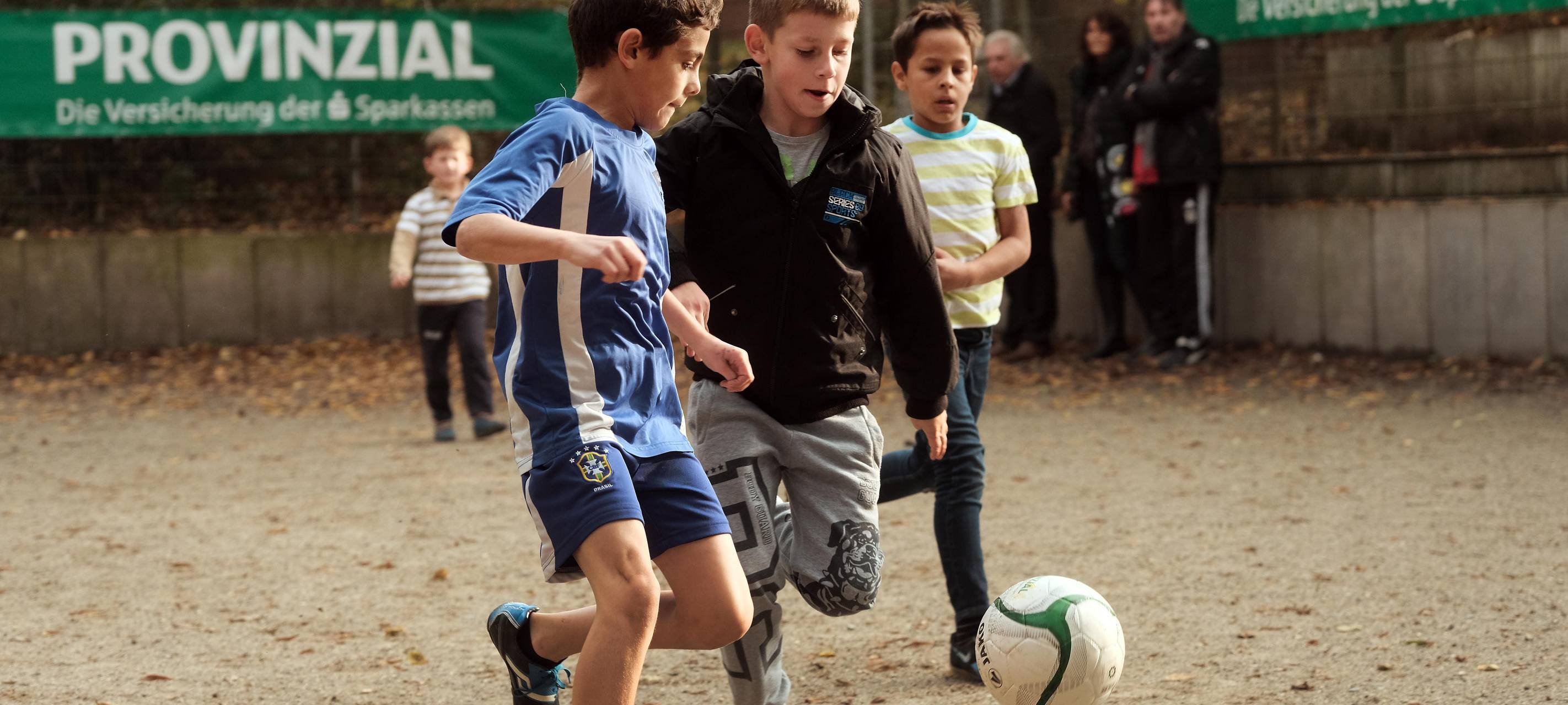 Kinder spielen Fußball auf einem Ascheplatz.