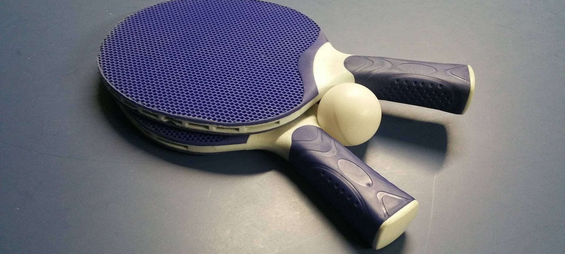 Zwei blaue Tischtennisschläger und ein Tischtennisball liegen mittig auf einer Tischtennisplatte.
