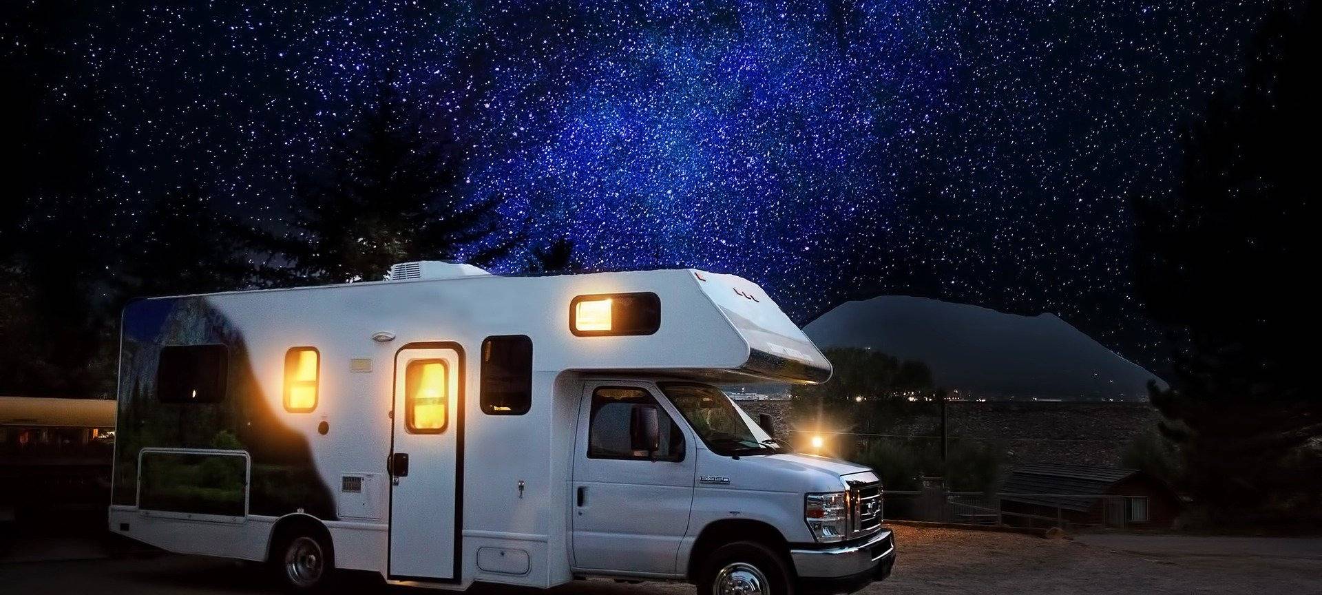 Ein Camper, bzw. Reisemobil steht beleuchtet auf einem Campingplatz. Es ist dunkel.