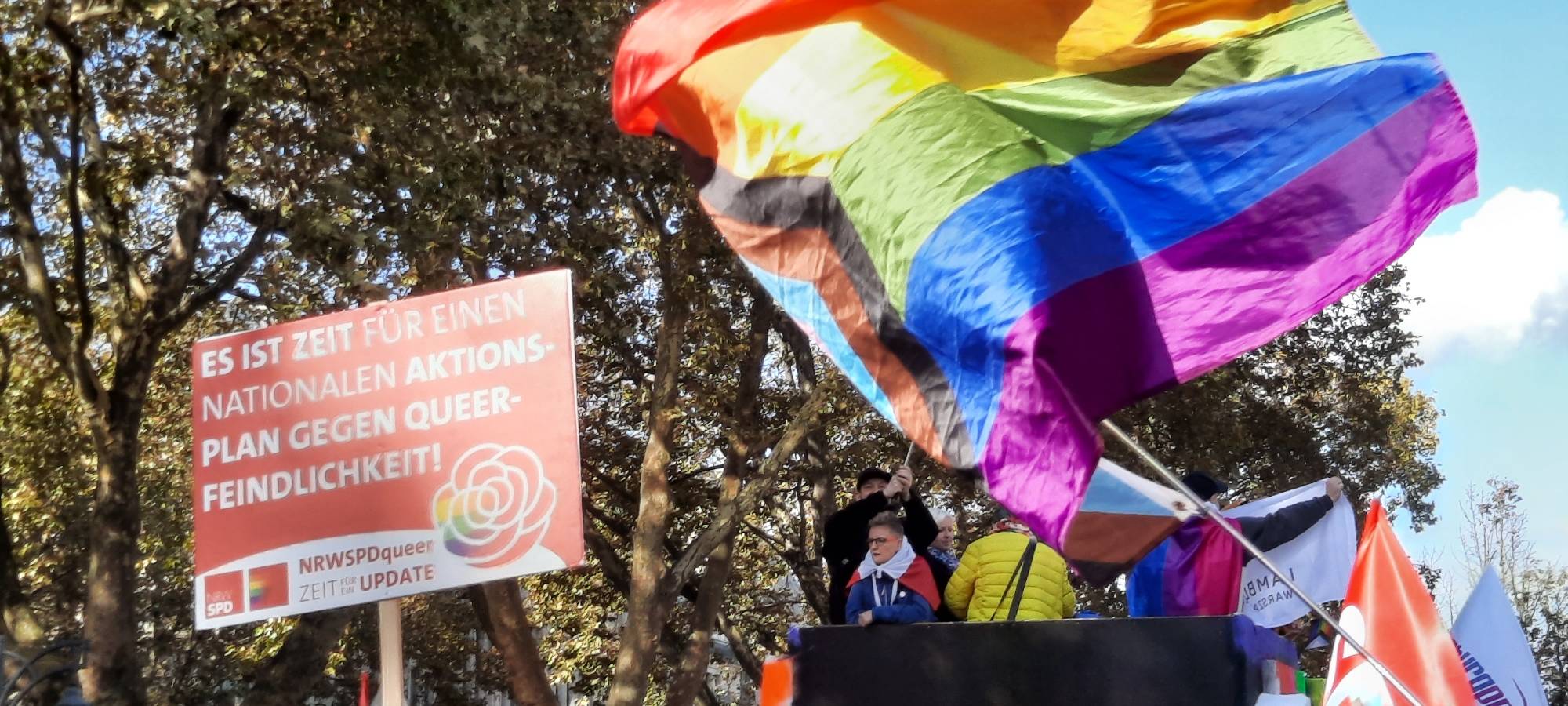 Eine Regenbogenflagge wehr bei einer Demo.