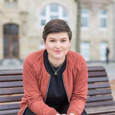 Sara Nanni vom Bündnis 90/ Die Grünen sitzt auf einer Bank und blickt in die Kamera.