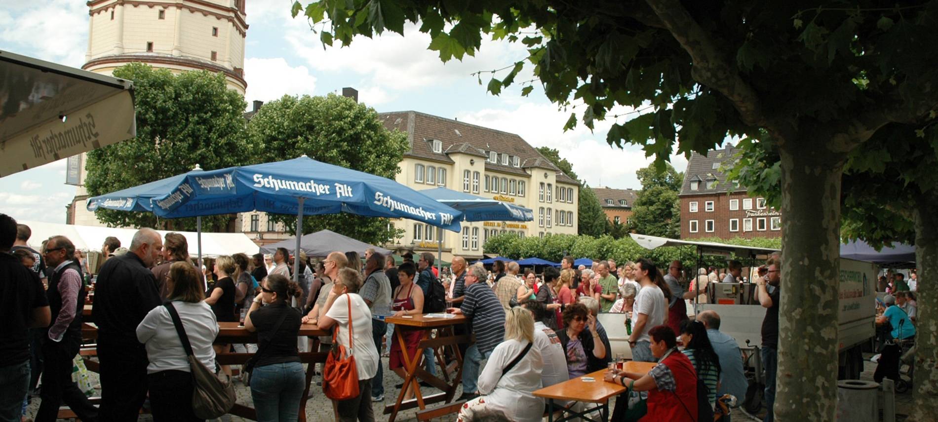 Menschen sitzen auf dem Burgplatz in Düsseldorf an Tischen.
