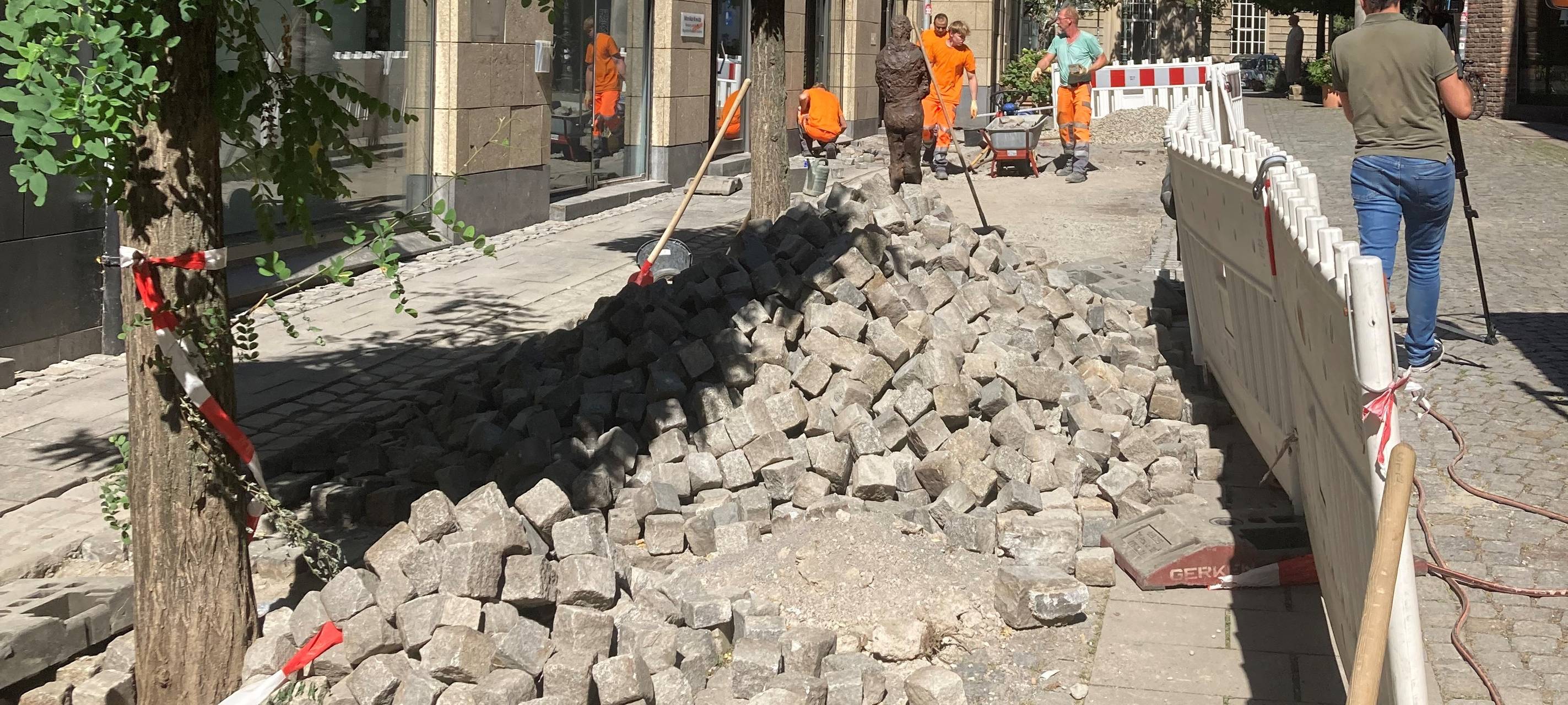 Im Vordergrund ein Haufen neues Pflaster für die Altstadt, im Hintergrund einige Bauarbeiter.
