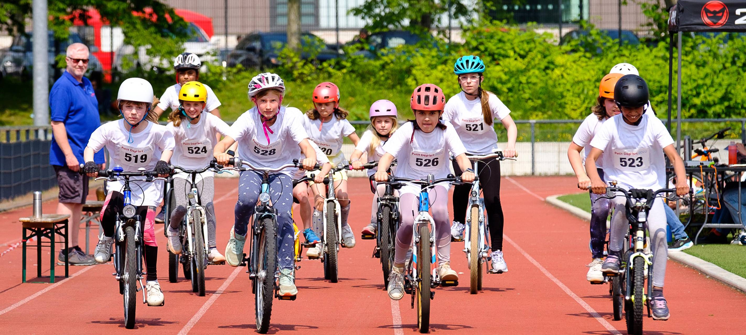 Kinder fahren mit Fahrrädern auf einer Laufbahn. Das Bild zeigt ein Rennen des Wettbewerbs Petit départ.