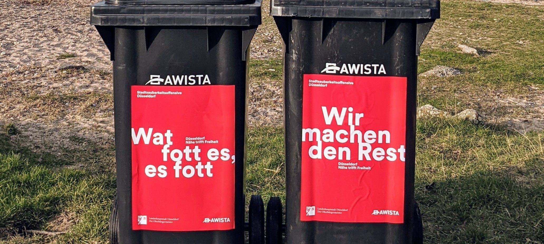 Zwei Mülltonnen, im Hintergrund ist Sand und Rasen zu sehen.