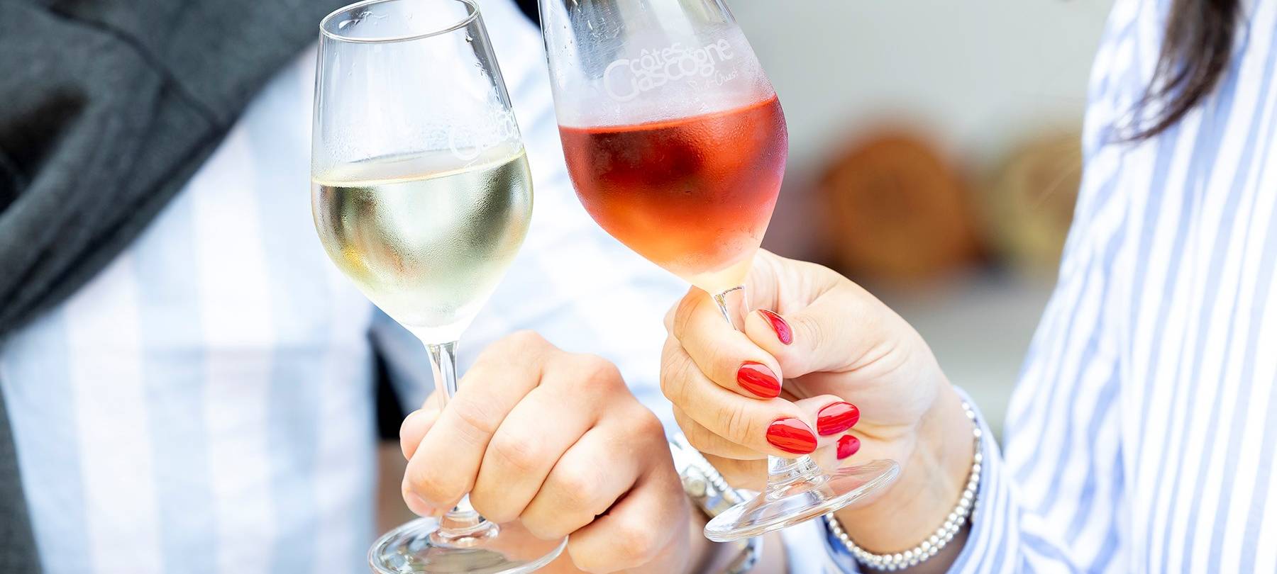 Zwei Weingläser stoßen aneinander, einmal Rotwein, einmal Weißwein