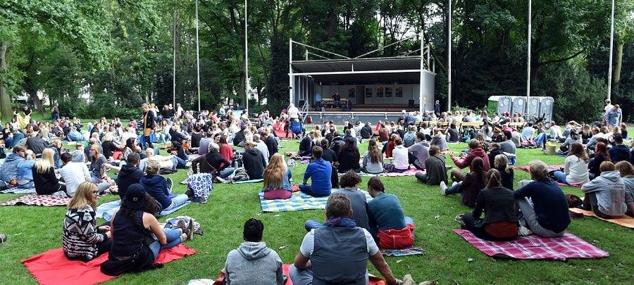 Poetryslam im Hofgarten. Menschen sitzen vor einer Bühne auf dem Rasen.