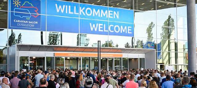 Willkommens-Schild zum Caravan Salon in Düsseldorf. Darunter sind viele Besucher zu sehen.