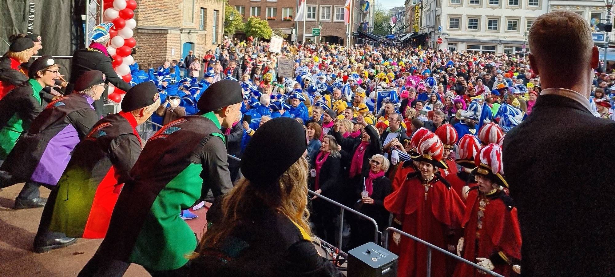 Auf dem Marktplatz vor dem Rathaus wird Karneval gefeiert. Auf einer Bühne macht die KG Regenbogen Stimmung.