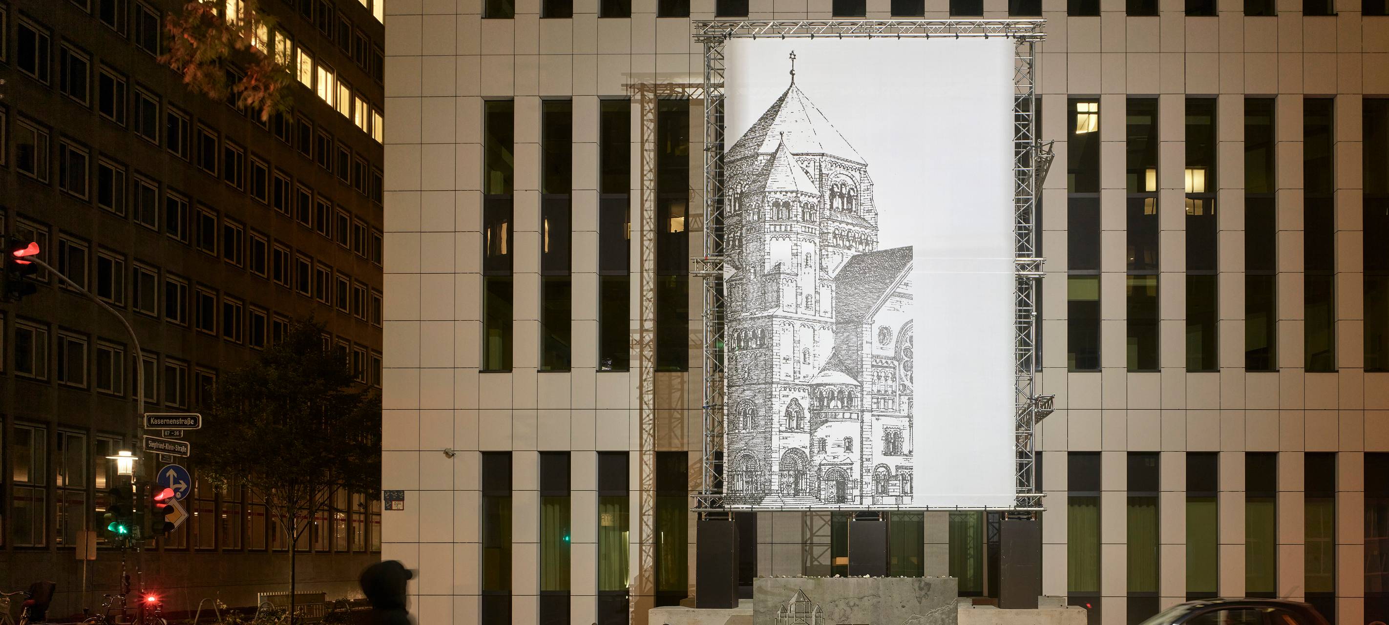 Die Lichtinstallation "missing link_" des Konzeptkünstlers Mischa Kuball. Zu sehen ist eine schwarz-weiß-Abbildung eines Teils der historischen Synagoge auf einer beleuchteten Glasplatte an einer modernen Gebäudefassade.