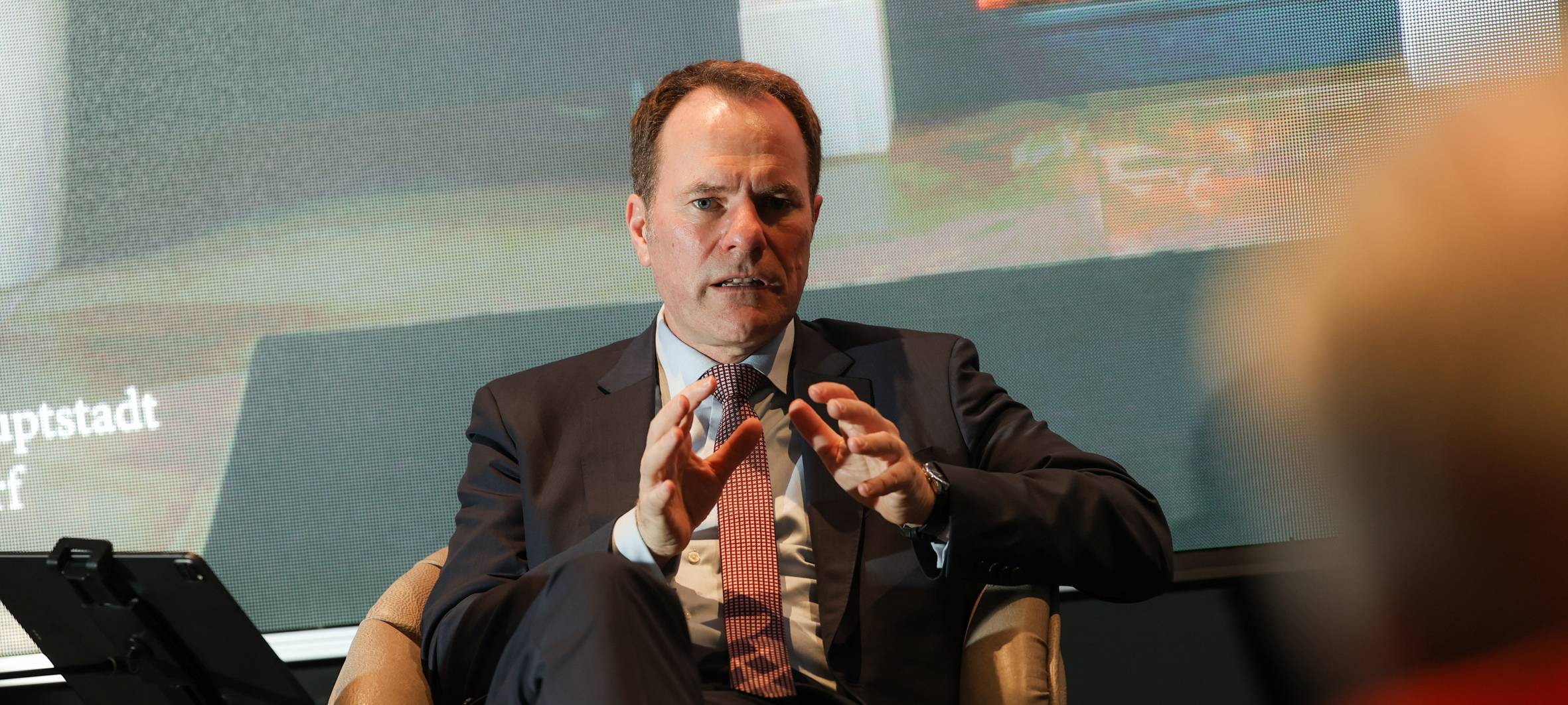 Oberbürgermeister Stephan Keller sitzt auf einem Podium und redet.