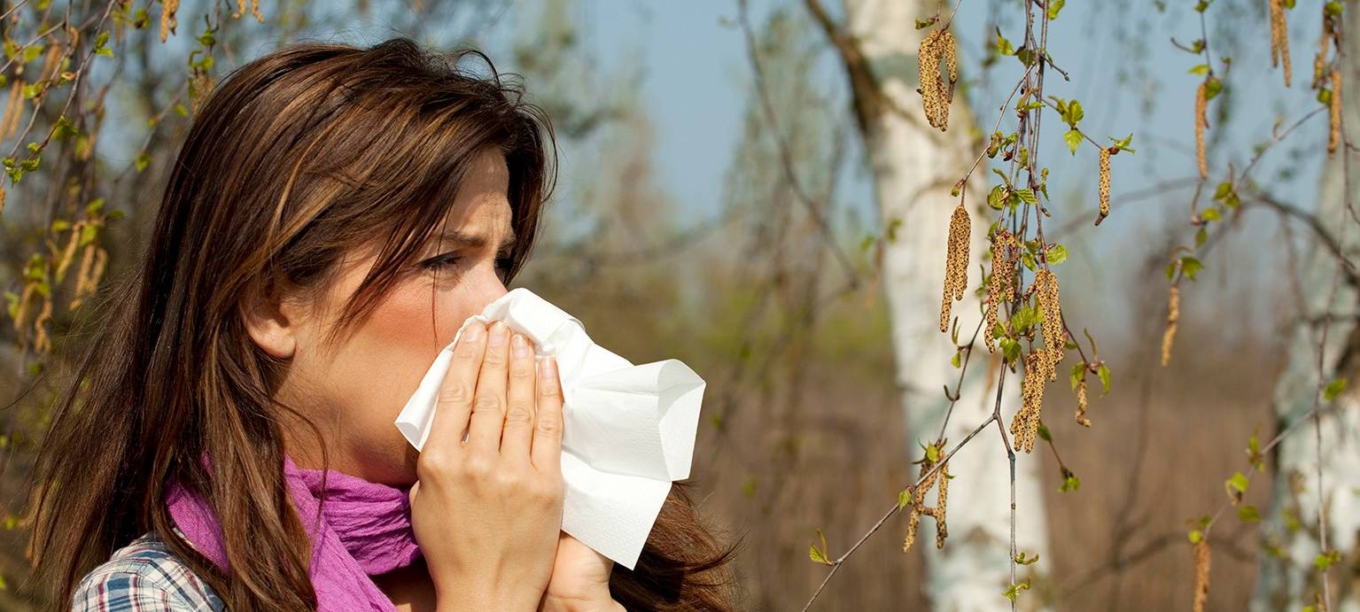 Eine Frau schnäuzt in ein Taschentuch. Sie hat Schnupfen, bzw. auch eine Allergie.