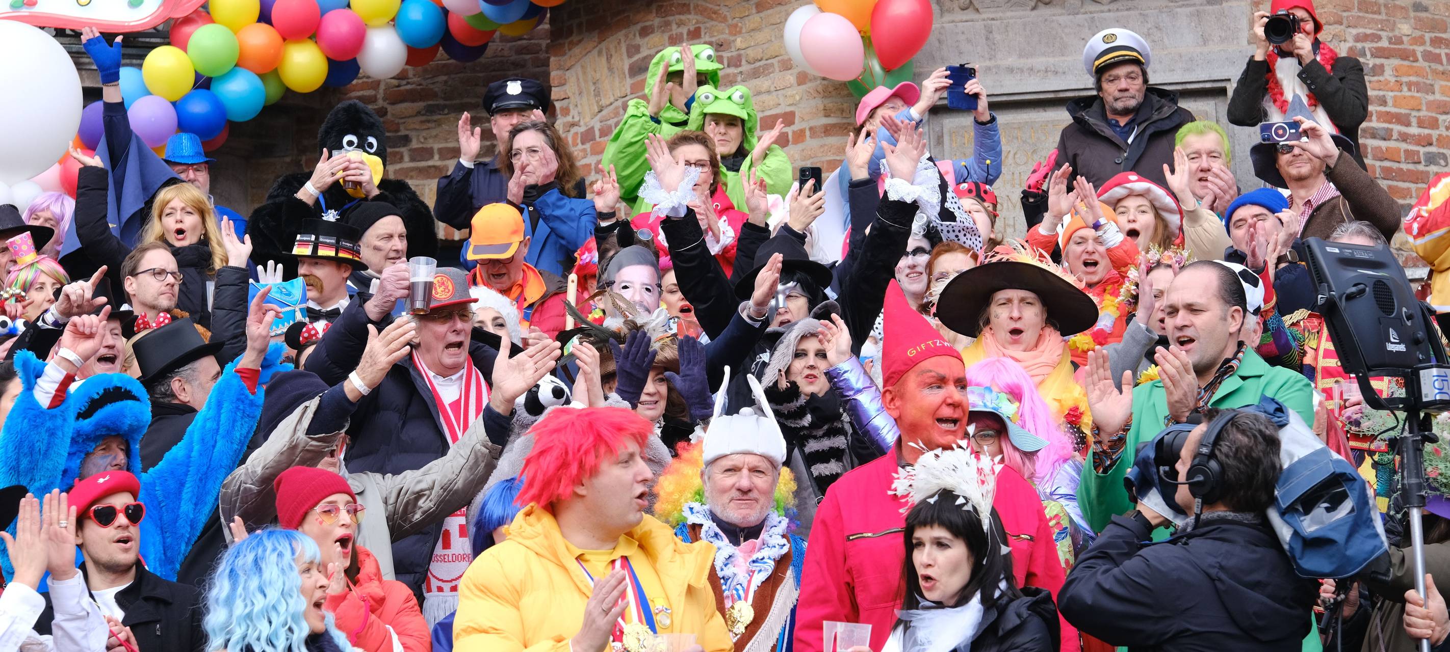 Eine vollbesetzte Tribühne vor dem Rathaus. Die Jecken feiern Rosenmontag und den Rosenmontagszug.