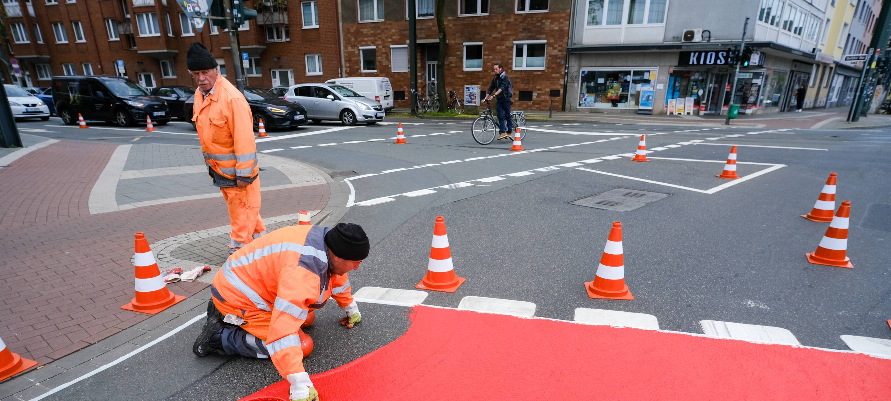 Ein Radweg wird rot markiert, zwei Bauarbeiter bei der Arbeit