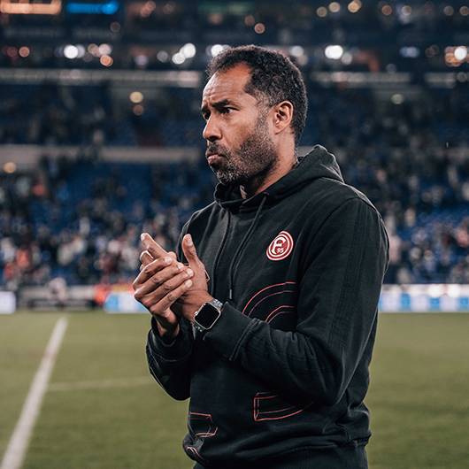 Daniel Thioune, der Fortuna-Trainer, steht auf dem Spielfeld und reibt sich die Hände.