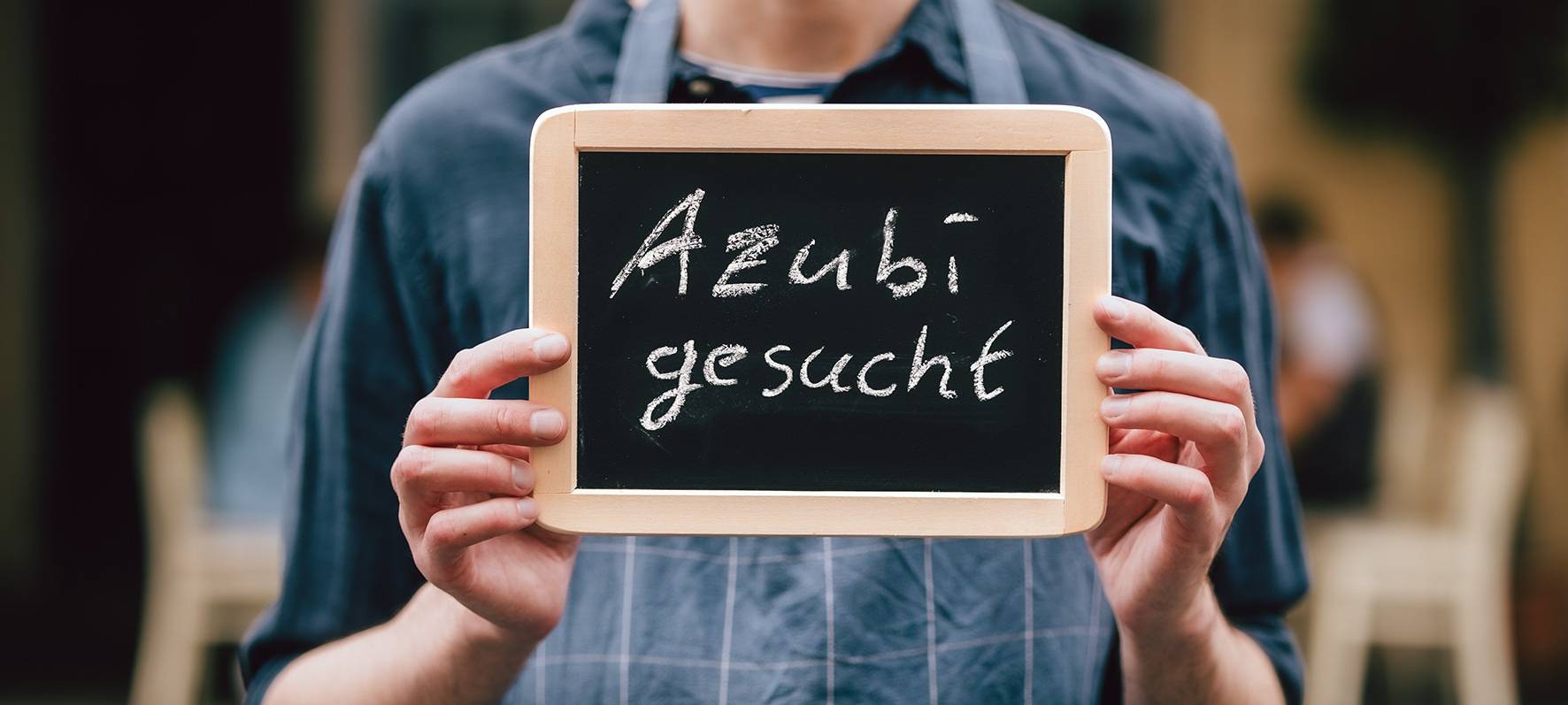 Ein Mann hält ein Schild mit der Aufschrift "Azubi gesucht".