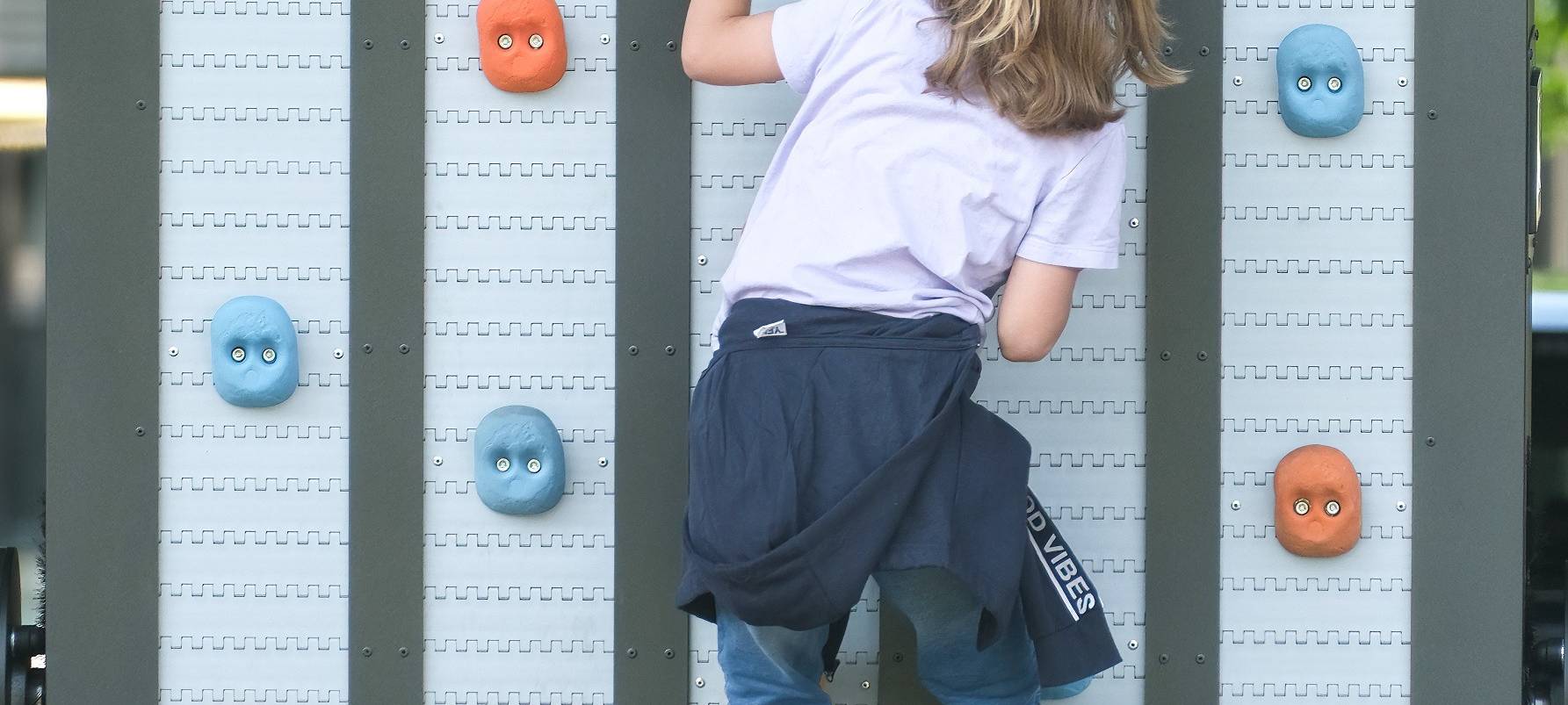 Ein Mädchen klettert an einer Kletterwand mit bunten Griffen. Das Angebot ist Teil des Olympic Adventure Camp am Rhein.