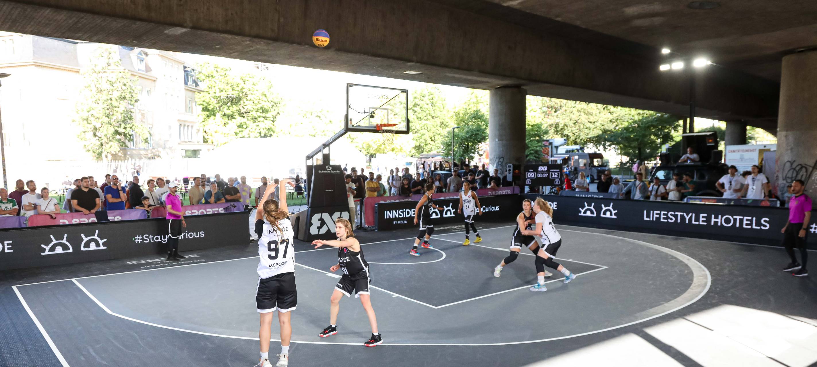 3x3-Basketball auf einem Court unterhalb der Rheinkniebrücke. Eine Spielerinn setzt gerade zum Wurf an.