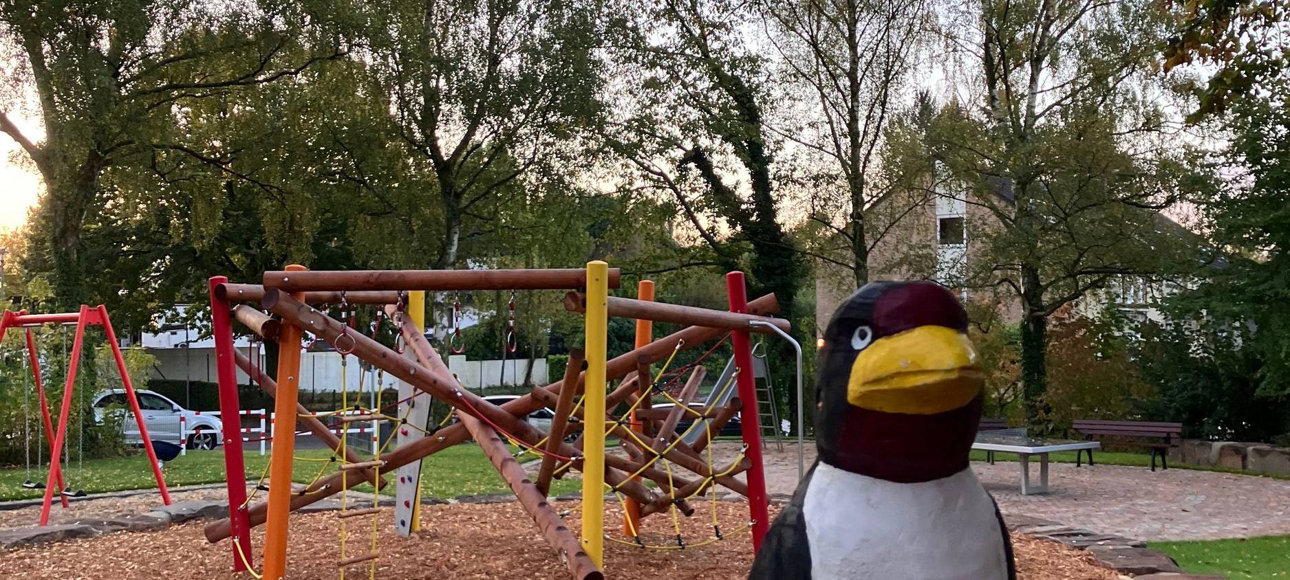 Eine Holzschwalbe auf einem Spielplatz in Düsseldorf Unterbach. Zu sehen ist auch ein Spielgerüst und Sand.